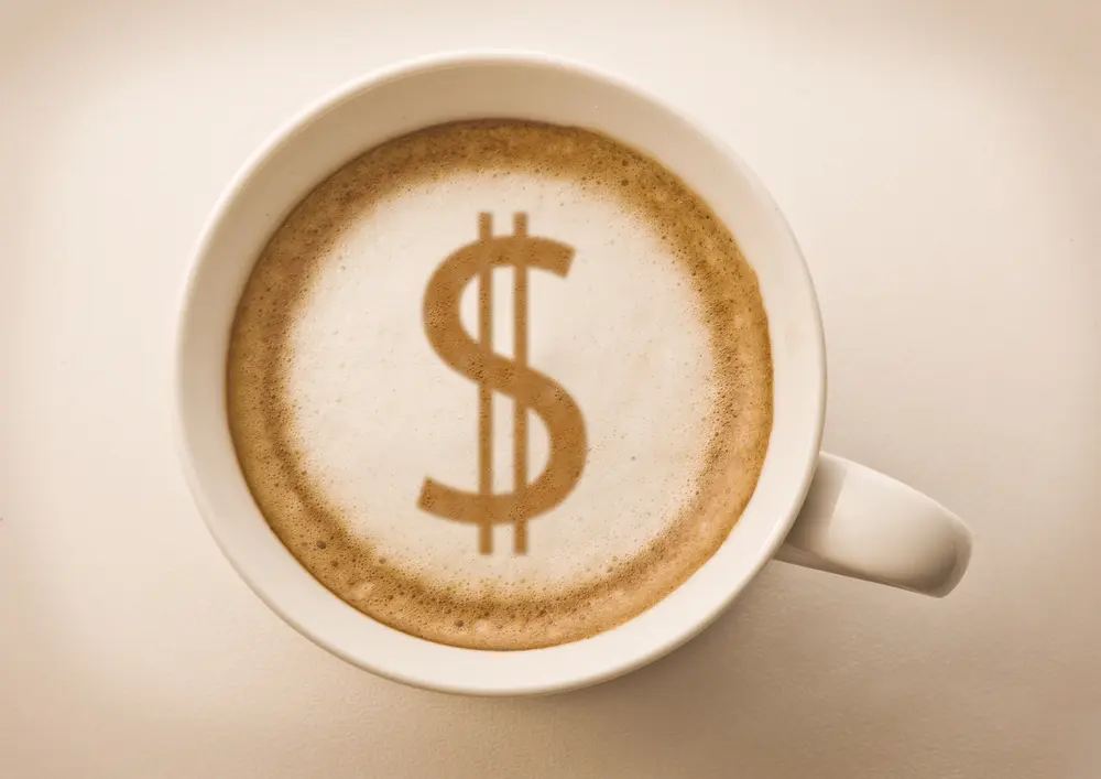 A latte in a coffee much with a dollar sign styled into the latte foam.