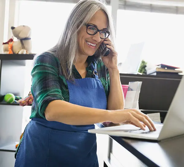 Woman wearing apron on phone looking at laptop