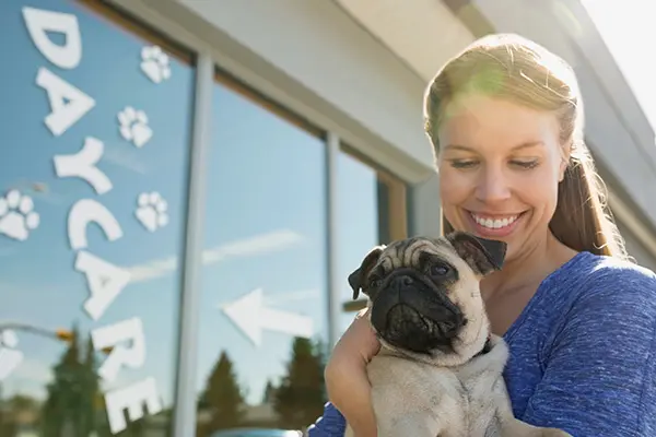 WOman holding pug dow outside of a dog daycare facility