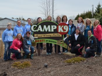 CampK9 award winning facility sign with the Camp K9 team posed around it.
