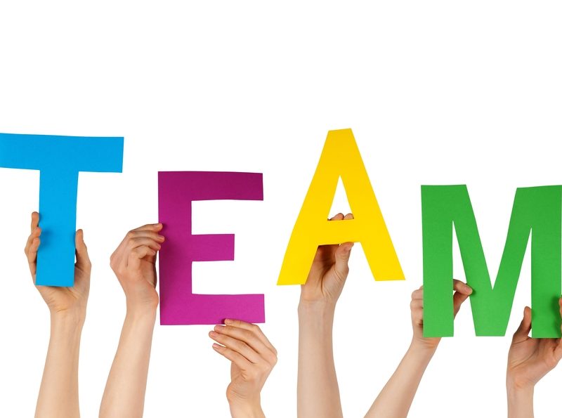 Six hands hold up blue, magenta, yellow, and green letters that spell out the word "team."