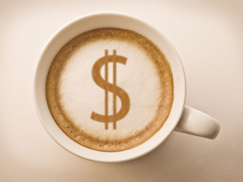 A latte in a coffee much with a dollar sign styled into the latte foam.