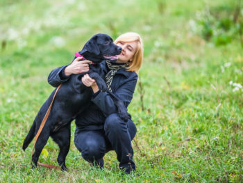 Woman holding black lab in a field